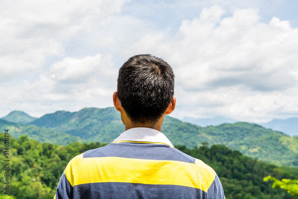 Naklejka premium A Chinese tourist looking at the landscape of mountain and green forest under sunlight near Kandy, Sri Lanka.