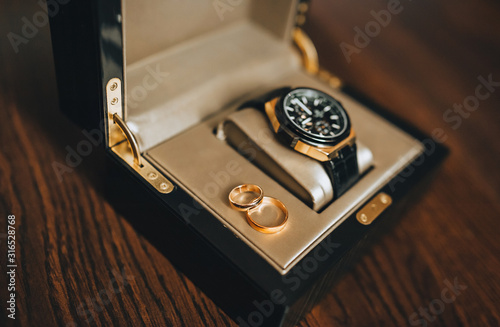 Wedding engagement gold rings in a box, case with an expensive watch close-up. Wedding accessories, details. The morning of the groom. Photography, concept.