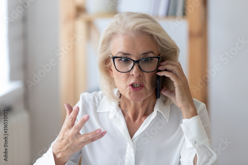 Mature businesswoman talking by phone arguing with client feels irritated photo