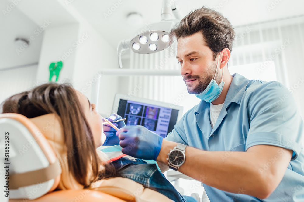 Dentist examining patient teeth with a mouth dental excavator. Close-up view on the woman's face