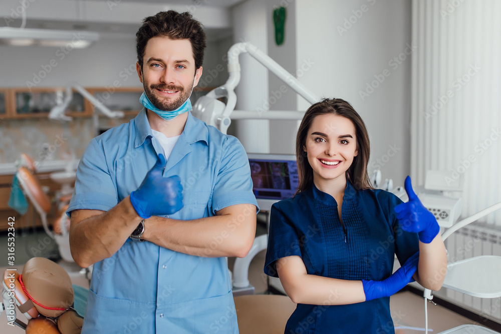 Obraz premium Portrait of smiling dentist standing with arms crossed with her colleague, showing okay sign.