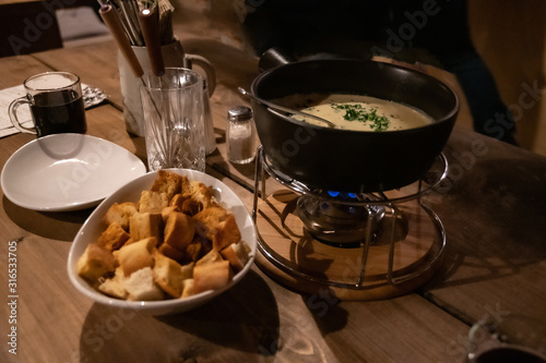 Rustic tablescape. Traditional French cheese fondue in hot pot and white bowl with bread crackers. Utensil atop wooden table. Winter hot food. Local cuisine. photo