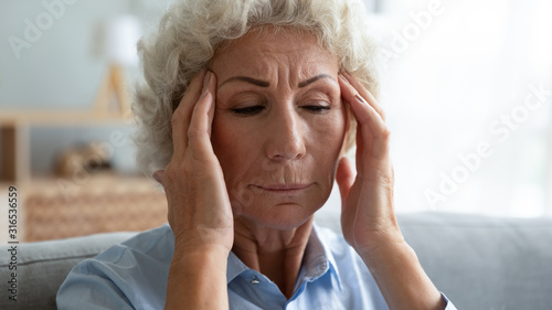 Close up unhappy older woman touching temples, suffering from headache