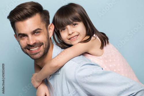 Happy young dad holding little preschool smiling daughter on back.