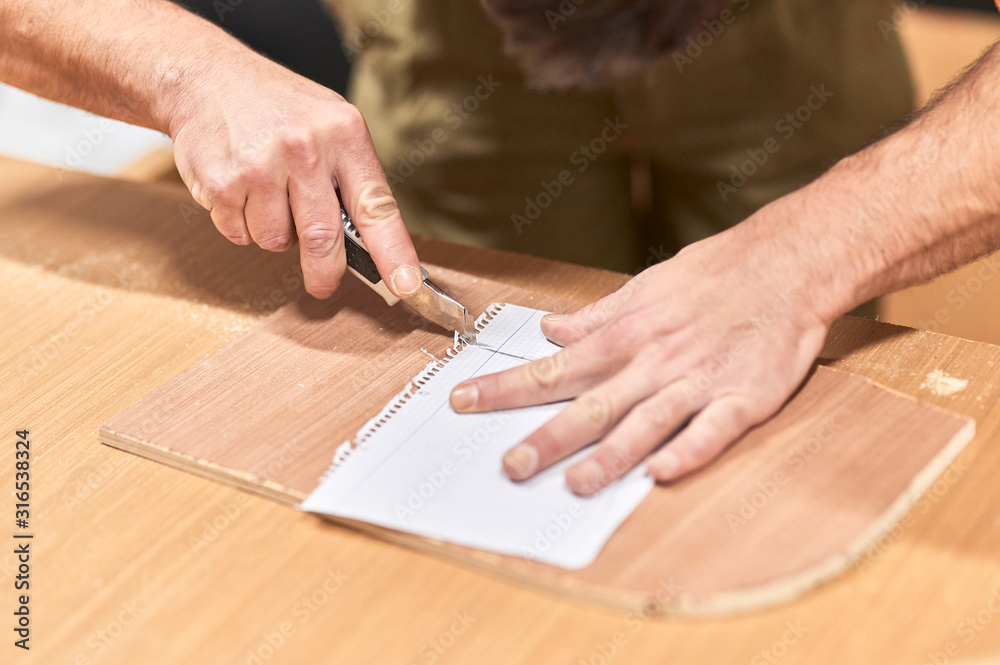 detail of hands cutting a paper template with a cutter on a wooden work table detail of hands cutting a paper template with a cutter on a wooden work table