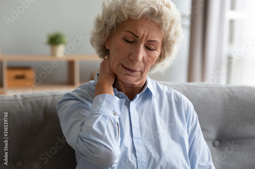 Unhappy older woman massaging tensed neck muscles, feeling unwell