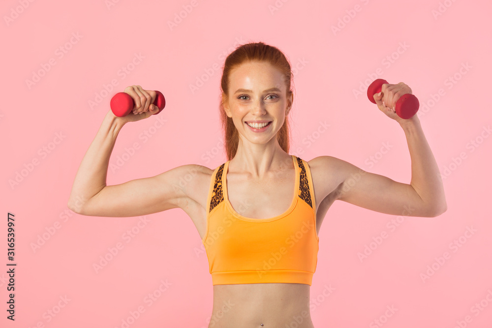 beautiful young woman with red hair on a pink background with dumbbells in hands beautiful young woman with red hair on a pink background with dumbbells in hands