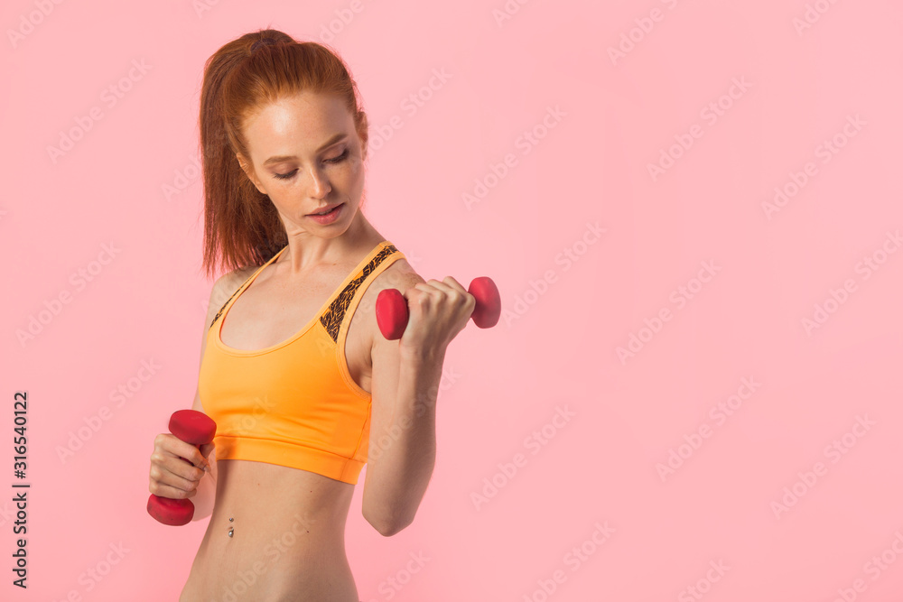 beautiful young woman with red hair on a pink background with dumbbells in hands beautiful young woman with red hair on a pink background with dumbbells in hands