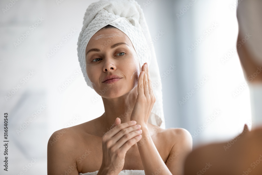 Head shot beautiful peaceful woman applying moisturizer on face Head shot beautiful peaceful woman applying moisturizer on face