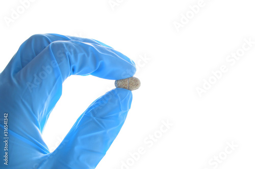 Hand holds a multivitamin complex pill horizontally. Wearing blue medical nitrile glove.