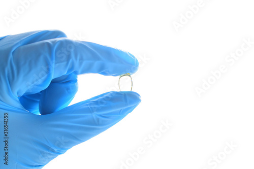 Hand holds a fish oil pill. Wearing blue medical nitrile glove.