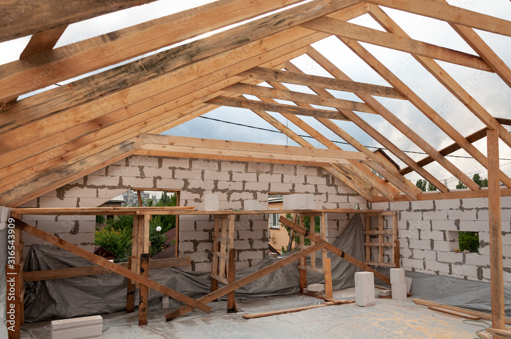 Installation of wooden beams. Rafter system on the mansard roof on a unfinished house building of the aircrete blocks Installation of wooden beams. Rafter system on the mansard roof on a unfinished house building of the aircrete blocks