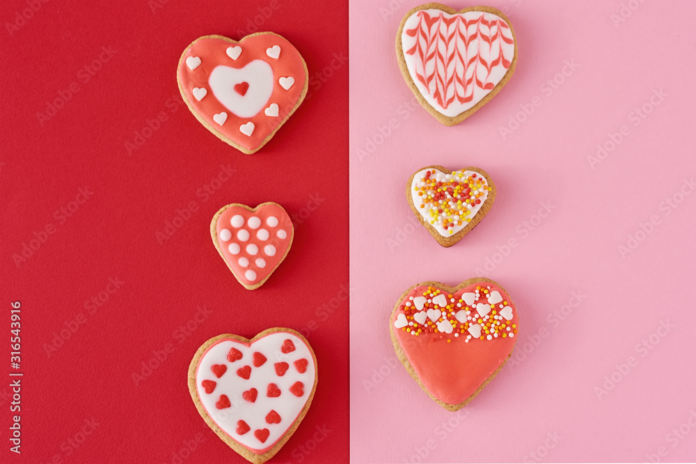 Fototapeta premium Decorated heart shape cookies on a colored red and pink background, top view