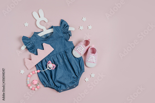 Blue dress on cute hanger with bunny ears and shoes, cotton crown and pacifier. Set of baby clothes and accessories for little Princess on pink background.  Fashion newborn. Flat lay, top view photo