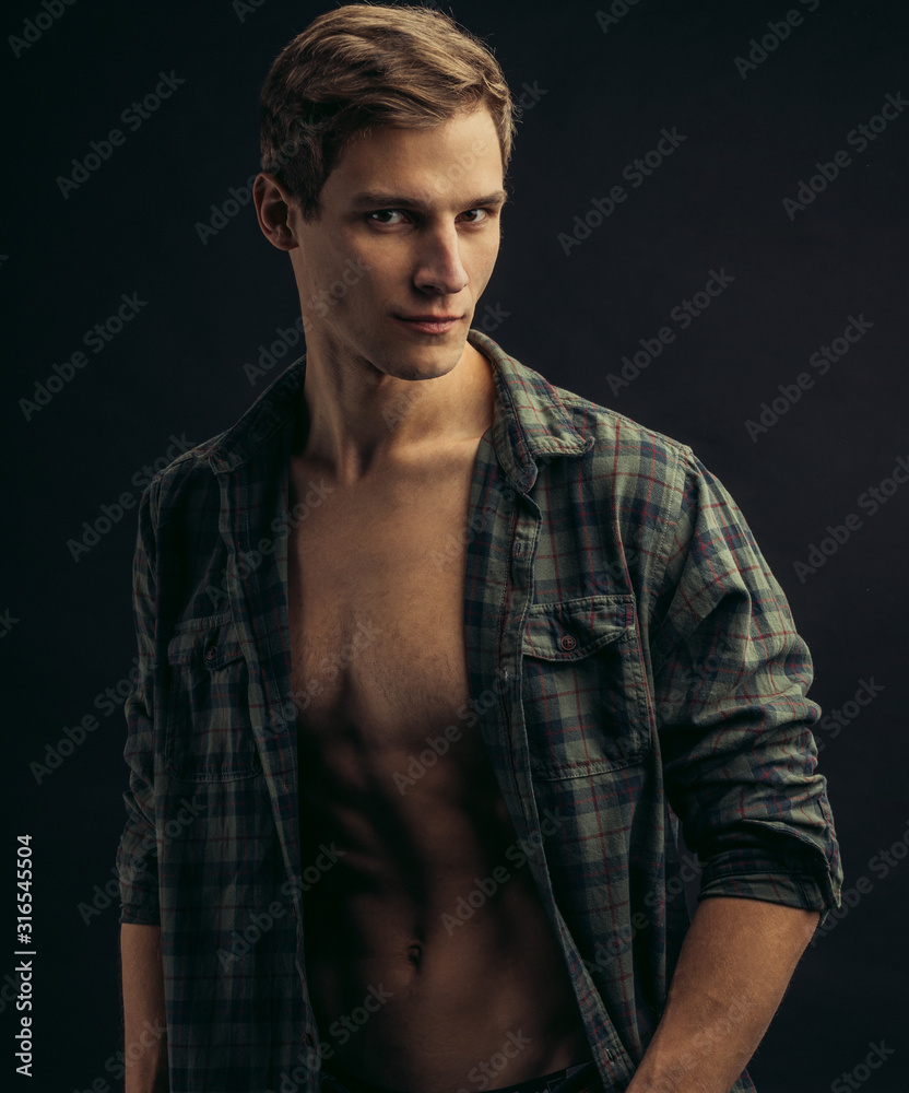 young caucasian man with muscular strong body opened torso, checkered casual shirt on him, he looks side isolated over black background