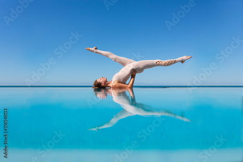 Graceful young woman a yoga lover doing Sarvangasana standing on the edge of the pool against the blue sky in a warm sunny day. The concept of improving blood supply to the brain, eyes and facial skin