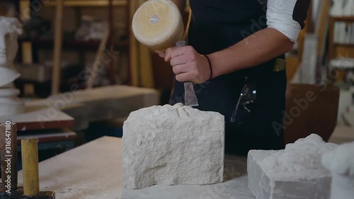 Close up of well-maintained male hands which creating from limestone the sculpture using chisel and mallet photo