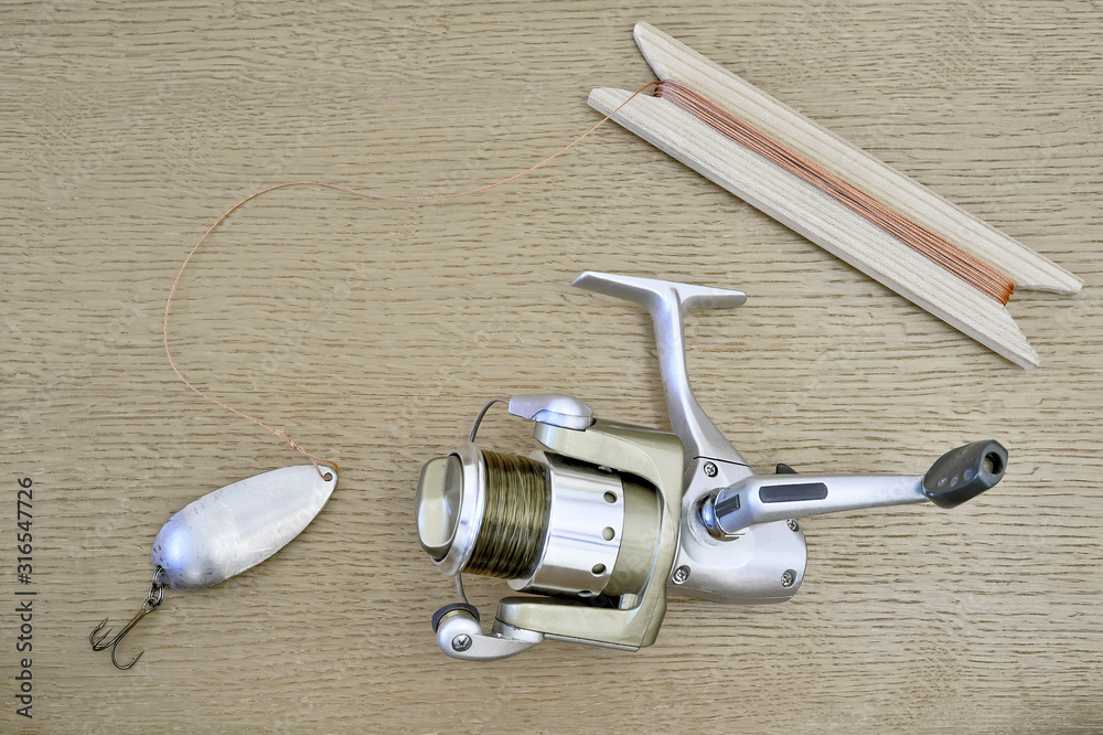 A modern spinning reel with a fishing line and a homemade spoon with a cord tied to it, wound on a wooden reel. A modern spinning reel with a fishing line and a homemade spoon with a cord tied to it, wound on a wooden reel.
