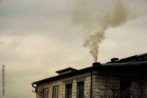 black smoke comes from chimney of a house against gray sky, heating with coal in winter. environmental problem of smog in Beskid Mountains, Zywiec, Krakow. heating system needs to be upgraded.