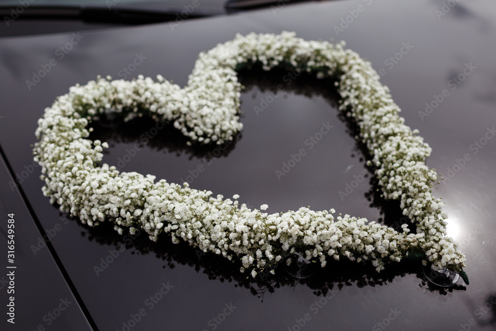 wedding car decorated with a heart of the white flowers