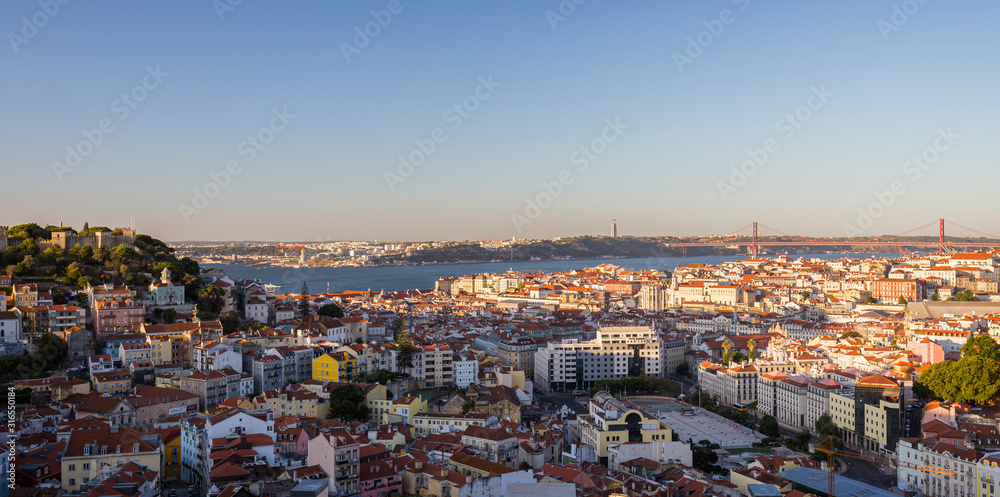 Panoramic city view from above of the Sao Jorge Castle (Castelo de Sao Jorge), downtown, Cristo Rei monument and 25 de Abril Bridge (25th of April Bridge) over Tagus River in Lisbon, Portugal.