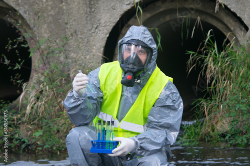specialist in a gray protective suit and mask, on the pond, takes a sample of liquid in test tubes, close-up