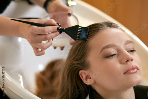 young beautiful woman dyeing hair in modern beauty saloon, professional hairdresser wash and dye woman's hair