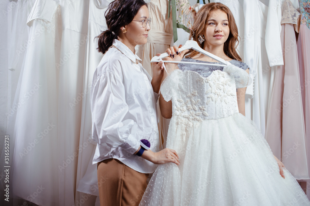 young caucasian bride going to buy wedding dress by designer in salon, try on it and look at mirror young caucasian bride going to buy wedding dress by designer in salon, try on it and look at mirror
