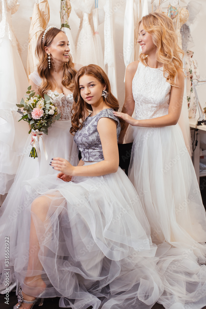 portrait of charming ladies future brides, wearing wedding dresses posing at camera together, beautiful young women of caucasian appearance in wedding salon