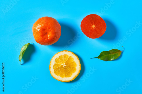 Scattered whole and pieces of mandarins or oranges, persimmon and green leaves on blue background. Fruit purchasing concept. Top view. Close-up