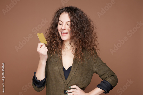 Фотография Excited fashionable female dressed in black bra and formal jacket being in high spirit about huge balance on credit cart, going to make great shopping online, isolated on beige studio background