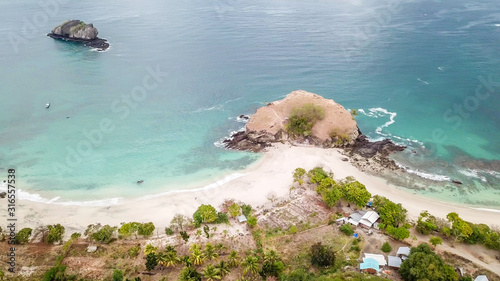 Fototapeta Naklejka Na Ścianę i Meble -  A top-down drone shot of an idyllic Koka Beach. Hidden gem of Flores, Indonesia. Headland going straight into the open sea. There is a small settlement next to the shore Calm waves washing the slopes