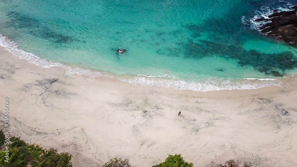 Top-down drone shot of an idyllic Koka Beach. Hidden gem of Flores Indonesia. Beauty in the nature. Calm waves washing the sandy shore gently. Serenity and calmness. There are some boulders in the sea