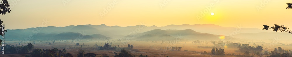 The beautiful panorama landscape of the sunrise, The sun's rays through at the top of the hill and the moving fog over the tree in the rice fields, Chiang Rai Northern  Thailand.