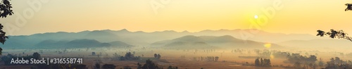 The beautiful panorama landscape of the sunrise, The sun's rays through at the top of the hill and the moving fog over the tree in the rice fields, Chiang Rai Northern Thailand.