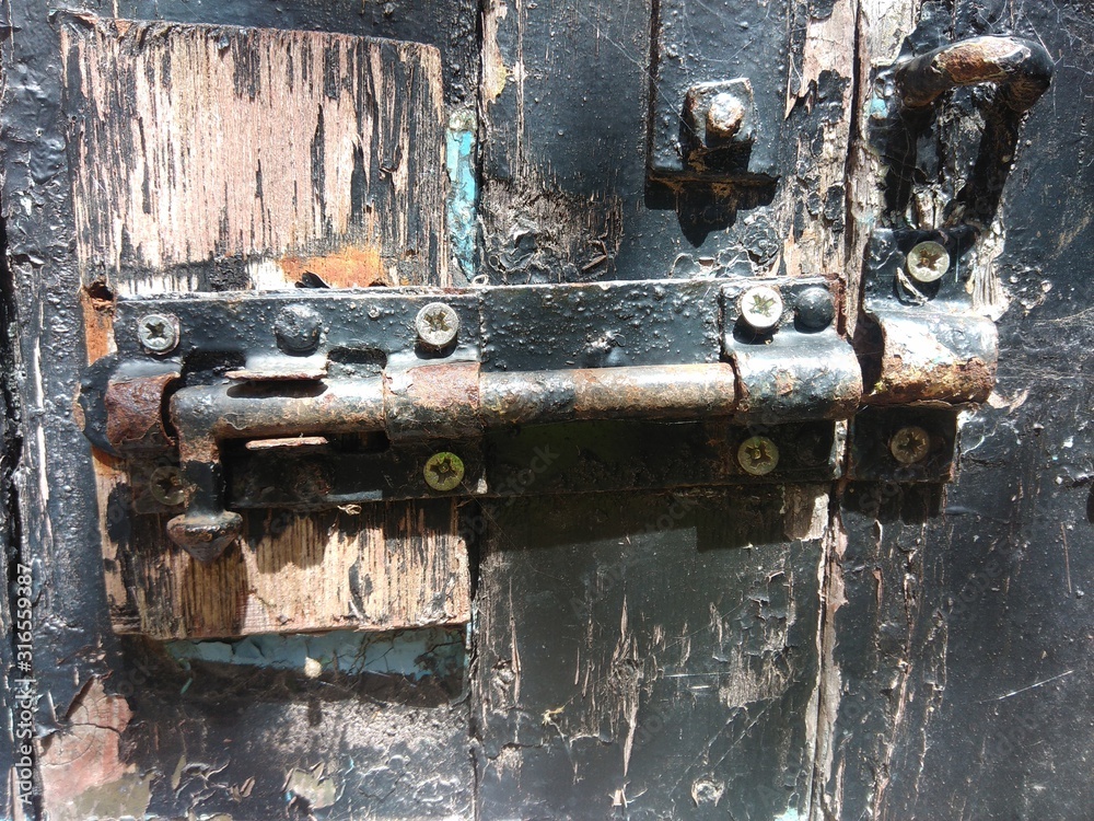 close-up of rusty metal bolt on peeling black paint wooden door