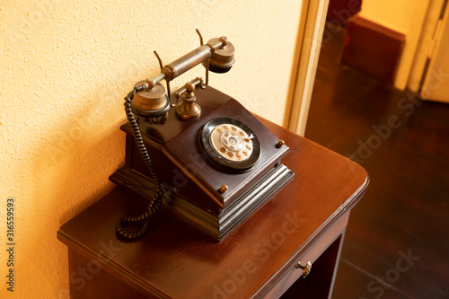 A classic Antique wooden telephone standing on a table against a yellow wall
