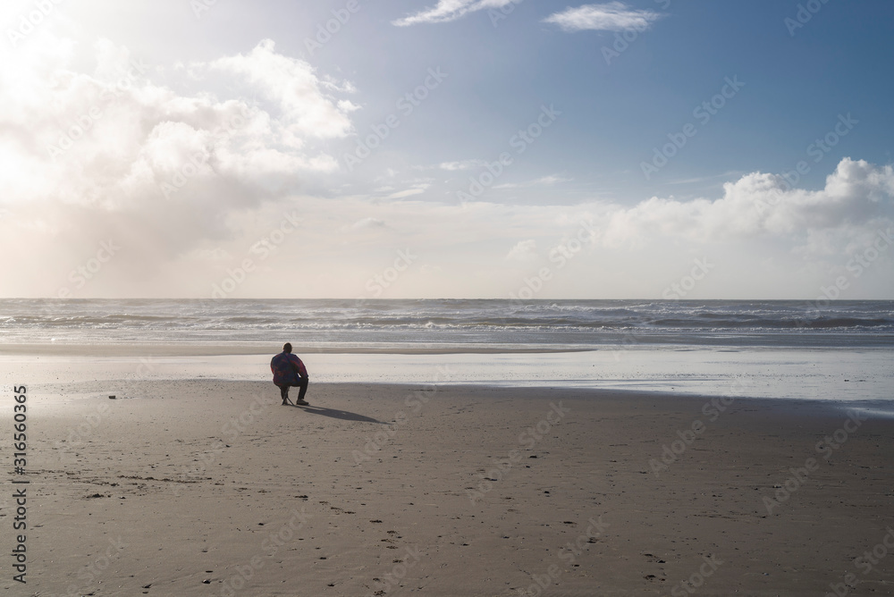 France; Picardie. Fort-Mahon. Un homme seul assis sur la plage regarde la mer. A lonely man sitting on the beach looks at the sea. France; Picardie. Fort-Mahon. Un homme seul assis sur la plage regarde la mer. A lonely man sitting on the beach looks at the sea.