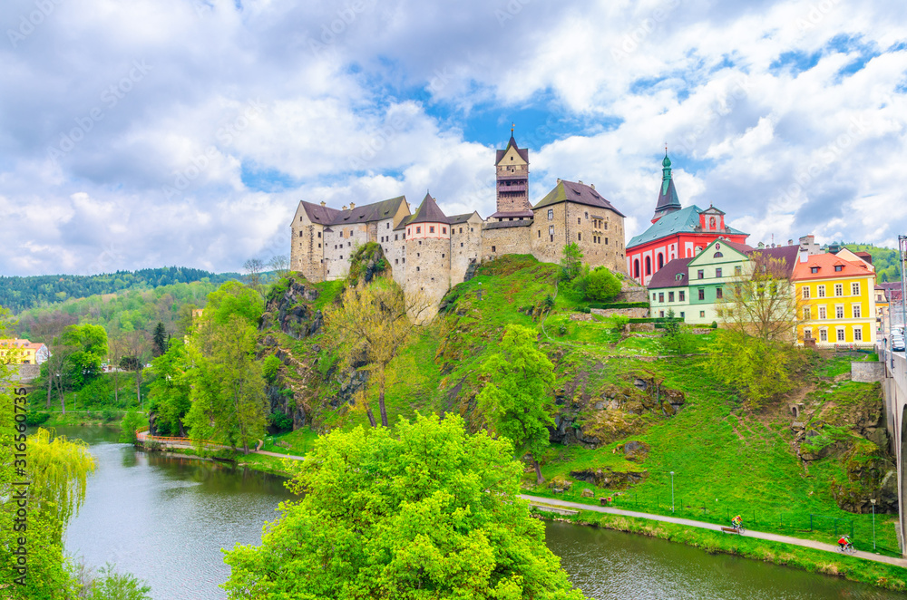 Loket Castle Hrad Loket gothic style building on massive rock over Eger river and colorful buildings in Loket town, green trees and hills background, Karlovy Vary Region, West Bohemia, Czech Republic