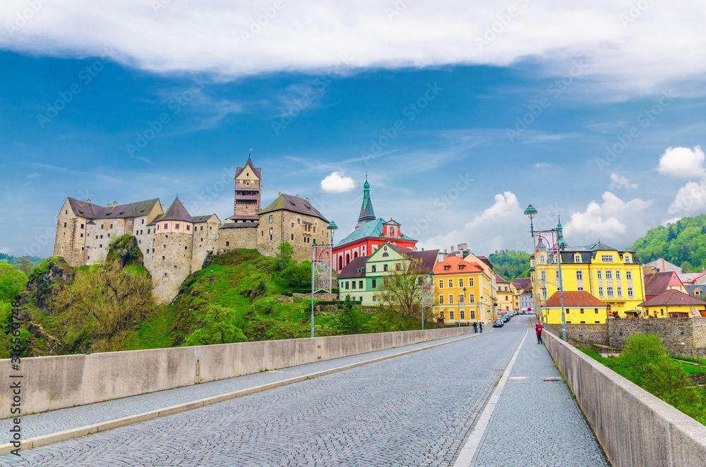 Obraz premium Loket Castle Hrad Loket gothic style building on massive rock, colorful buildings in town, bridge over Eger river, blue cloudy sky background, Karlovy Vary Region, West Bohemia, Czech Republic