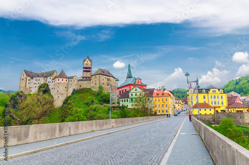 Loket Castle Hrad Loket gothic style building on massive rock, colorful buildings in town, bridge over Eger river, blue cloudy sky background, Karlovy Vary Region, West Bohemia, Czech Republic