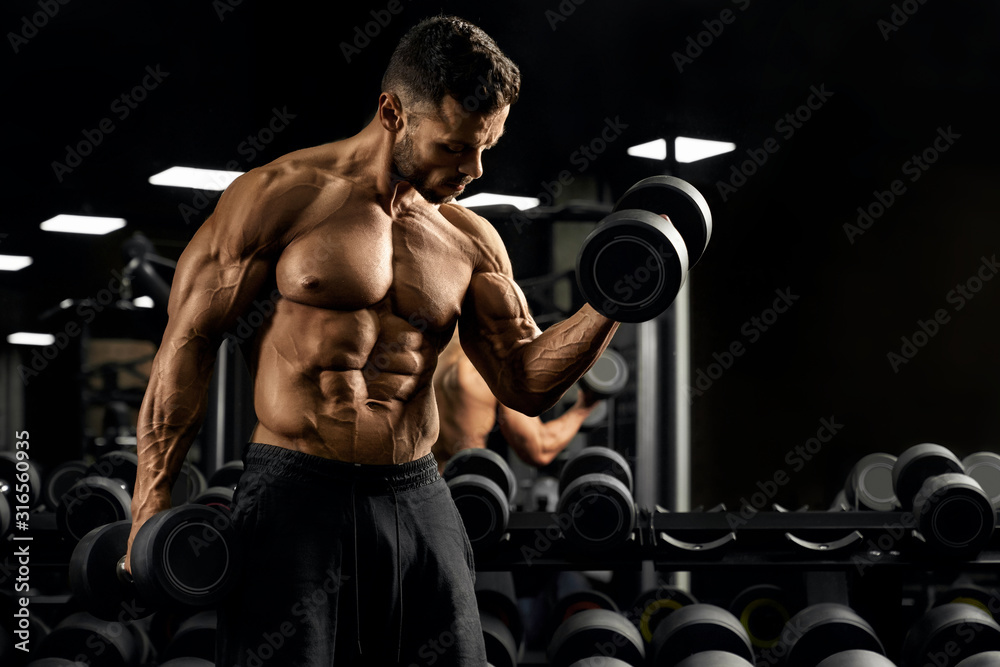 Muscular sportsman building biceps with dumbbell.
