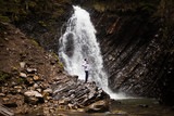 Female hiker walk near big mountains waterfall.