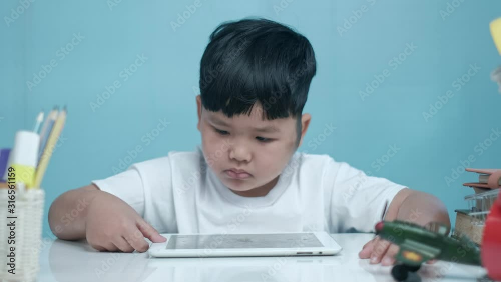 Little Asian boy using digital tablet on white desk in home, Education concept. Little Asian boy using digital tablet on white desk in home, Education concept.