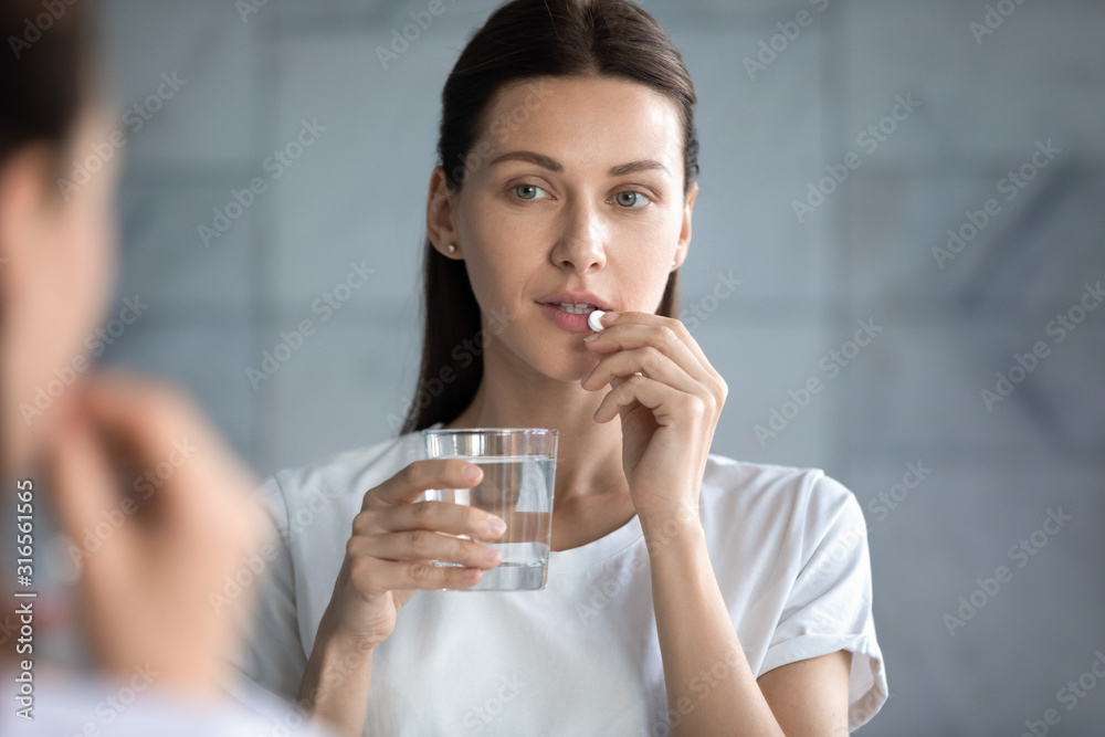 Head shot beautiful woman taking pill, looking in mirror Head shot beautiful woman taking pill, looking in mirror