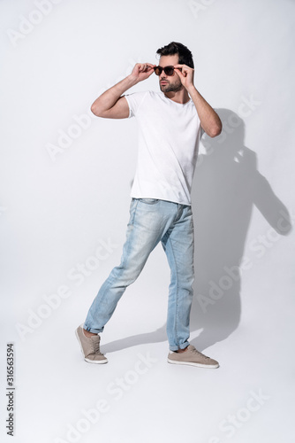 Full length of handsome young man in eyewear and casual wear looking away while standing against grey background © Roman