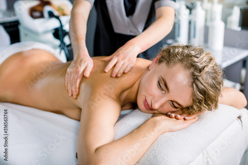 Relaxed happy woman receiving back massage at spa. An attractive caucasian woman getting classic massage in a spa center