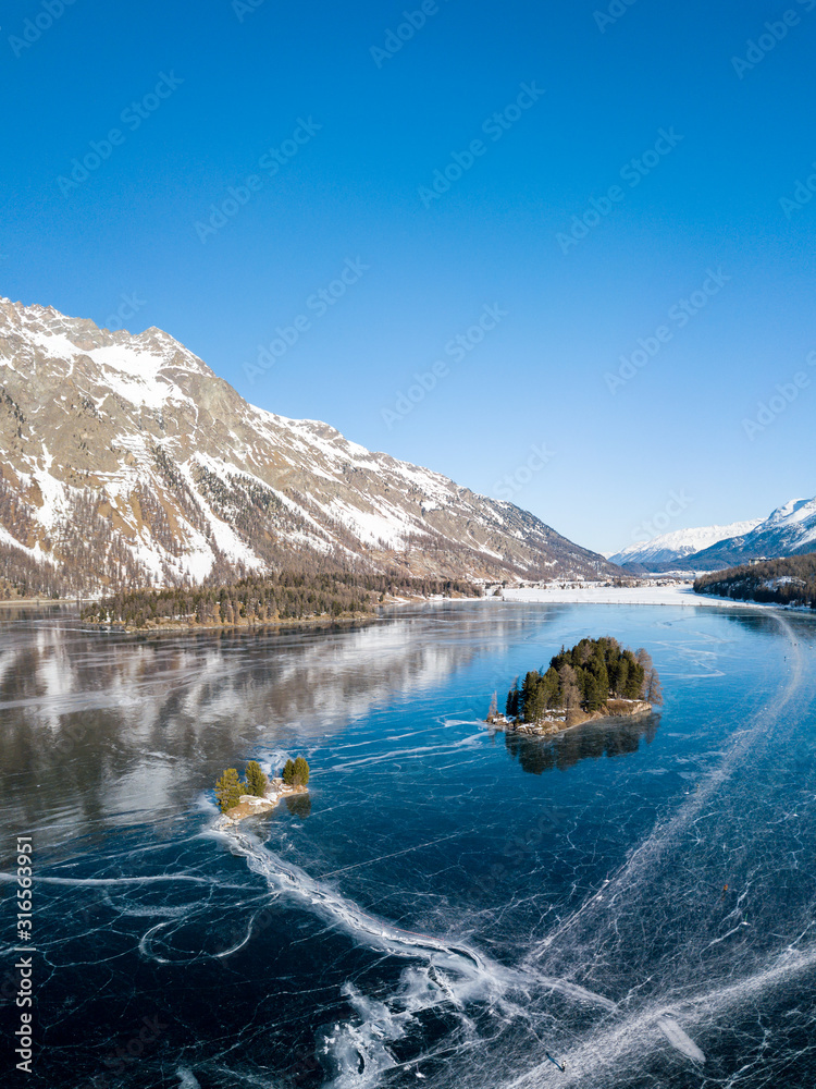 Obraz premium Aerial image of the Chaviolas islets on the frozen lake of Silsersee in St. Moritz, Switzerland