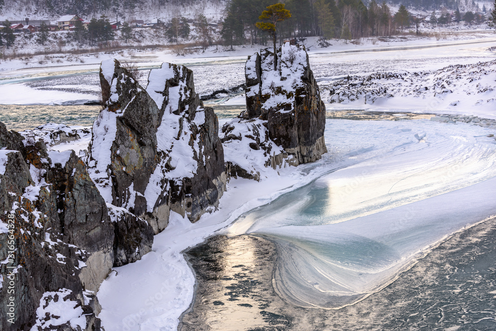 snow-covered rocks in the middle of a freezing river, illuminated by the sun