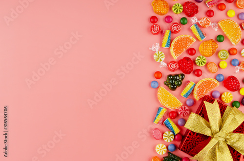 Flat lay view at sweet background of different type color and taste candies and gift box on pink. Space for text